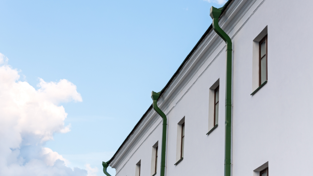 White building with green gutters and downspouts against a clear blue sky.