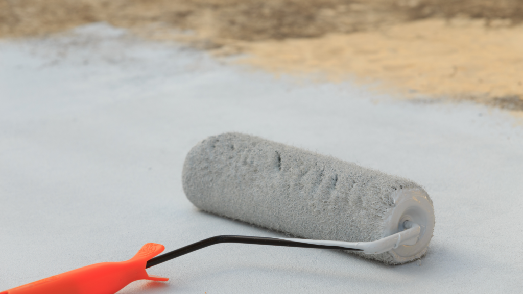 A paint roller and brush resting on a concrete floor, ready for a painting project.