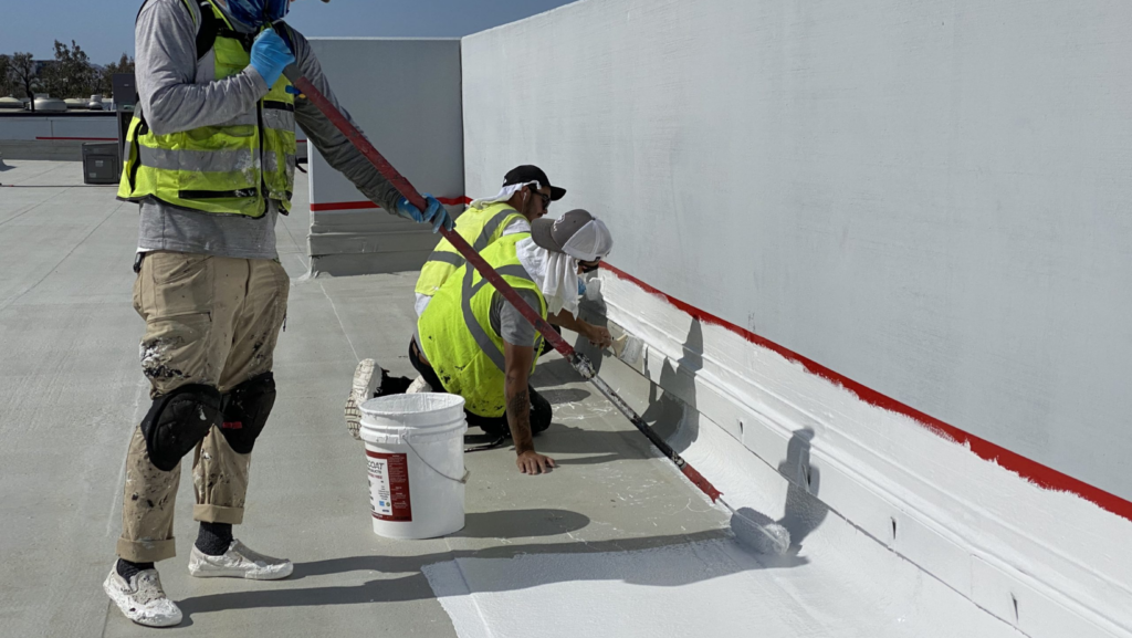 3 men applying white paint to a wall, showcasing teamwork in a commercial roofing project.