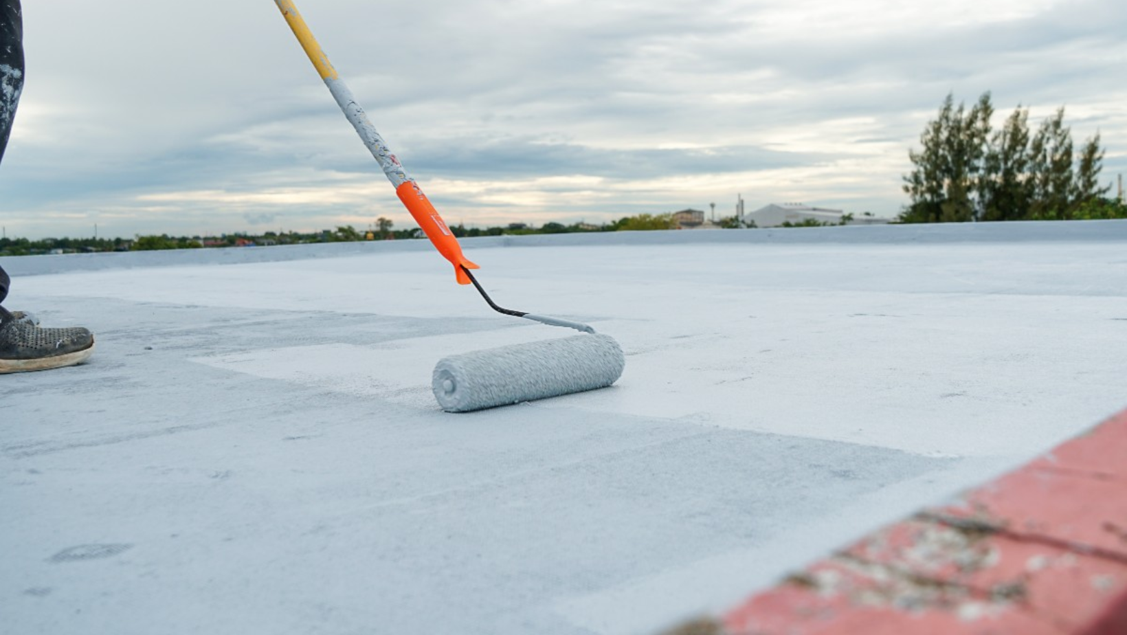 A man applies roof coating using a roller, ensuring even coverage on the surface above him.