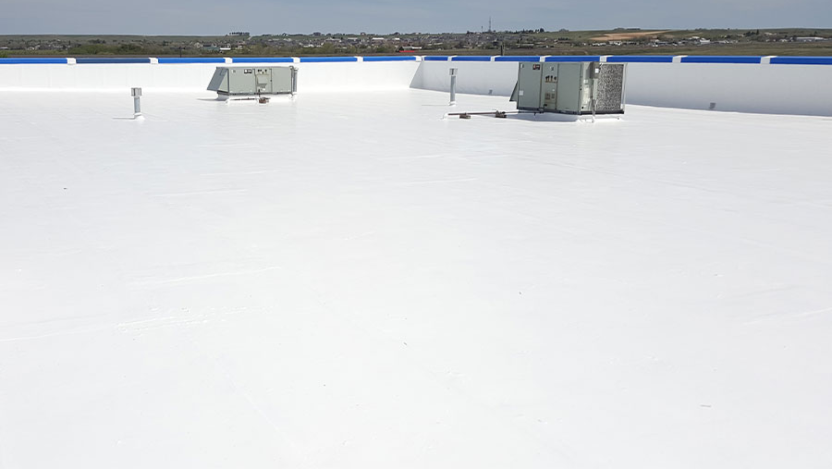 A white roof featuring a blue stripe, showcasing the roof coating installation process in progress.