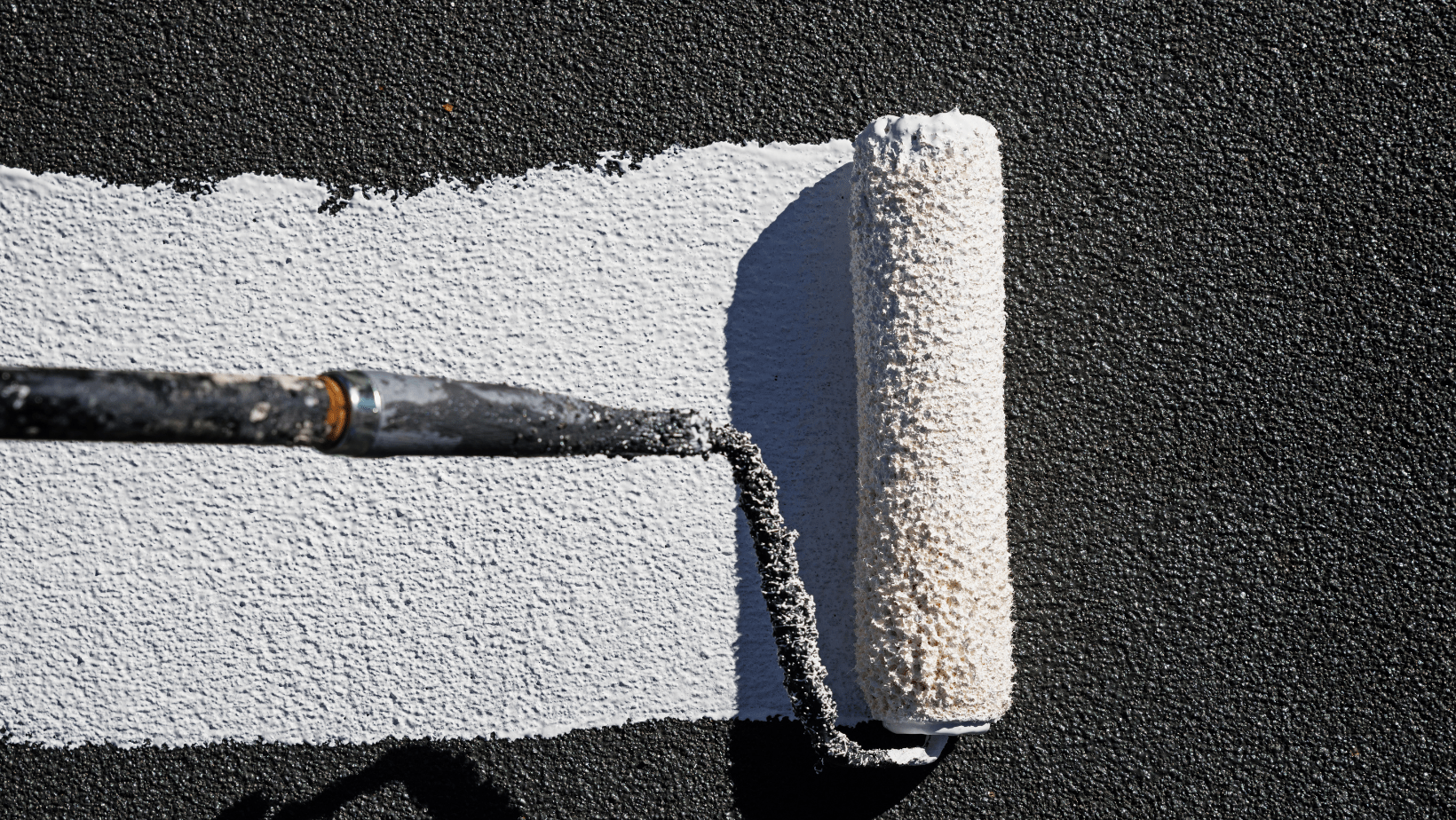 A roller is applying roof coating to a wall, showcasing the painting process in action.