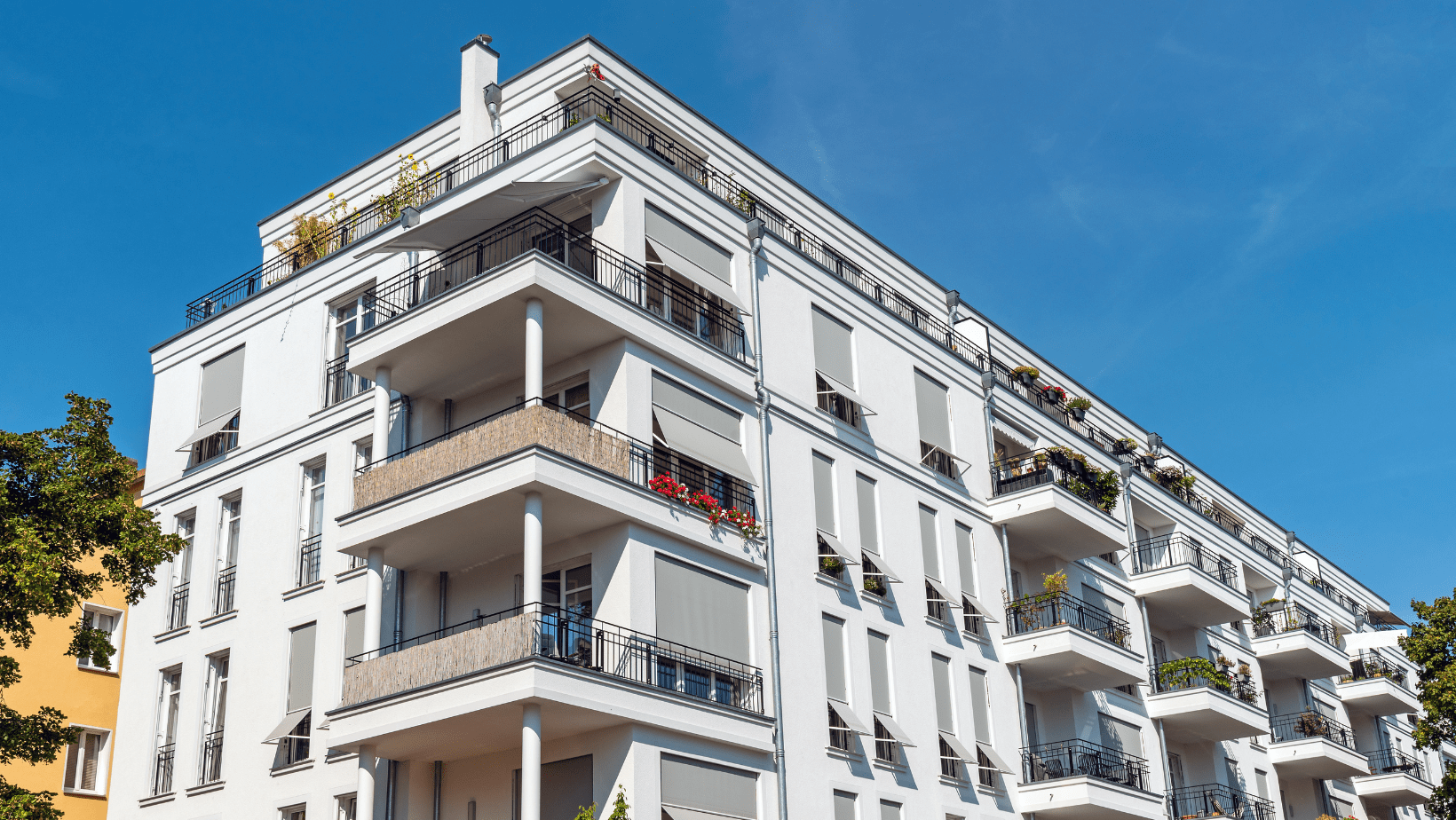 A white apartment building featuring multiple balconies along its side, showcasing a modern architectural design.