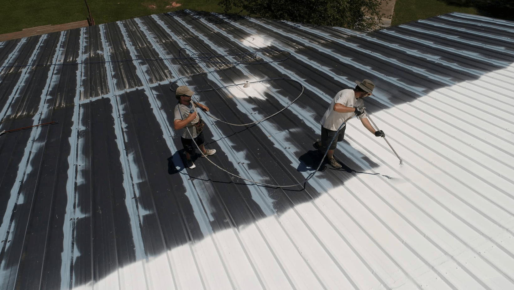 Two men applying spray paint to a metal roof, showcasing a vibrant transformation of the surface.