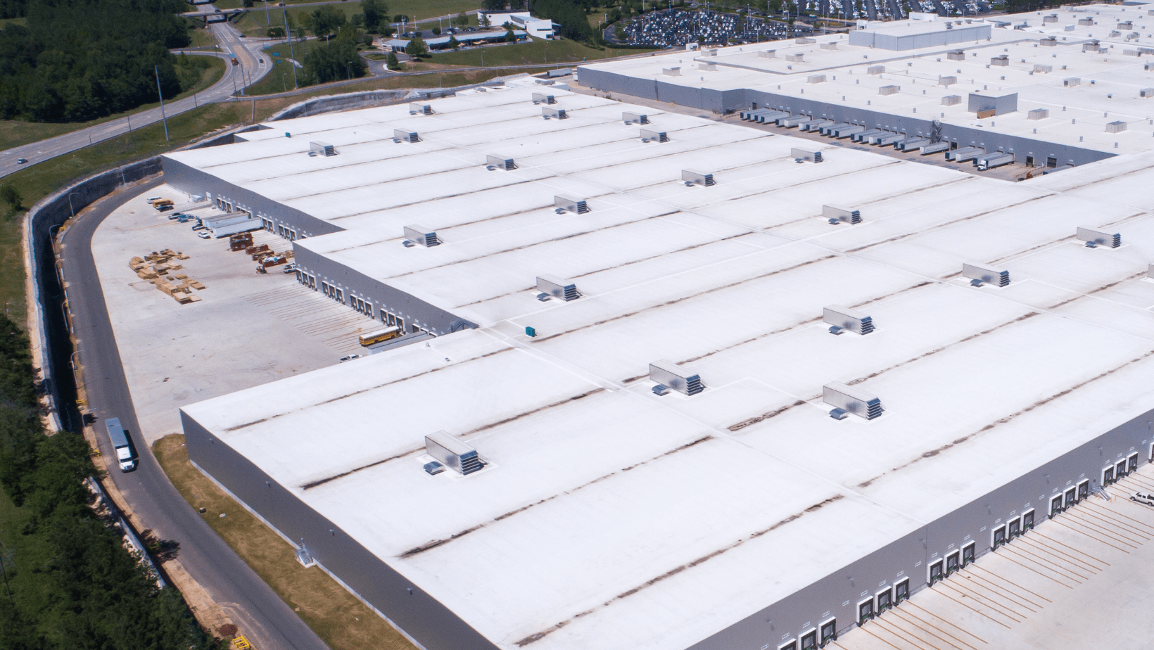 Aerial view of a large warehouse complex featuring numerous white roofs under a clear blue sky.