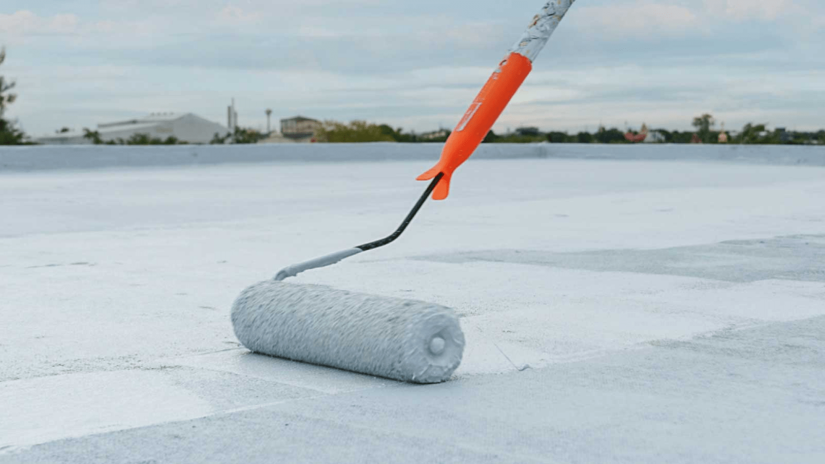 A person using a roller to apply paint on a roof, showcasing the process of roof maintenance and improvement.