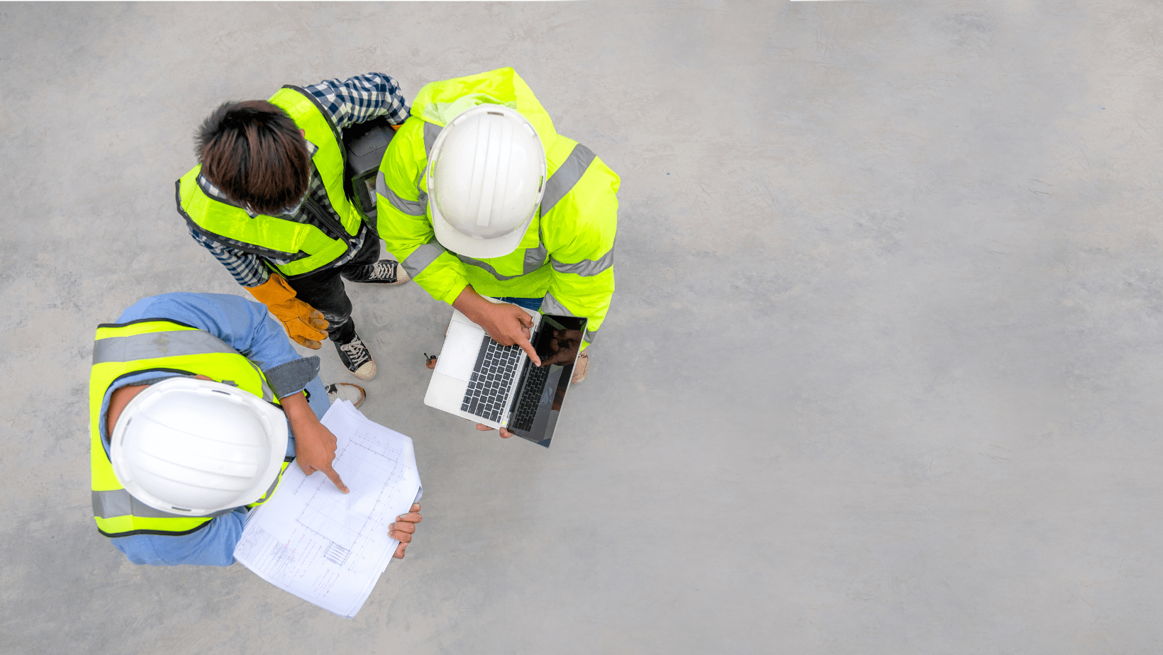 Three construction workers wearing hard hats and safety vests, collaborating on a building site.