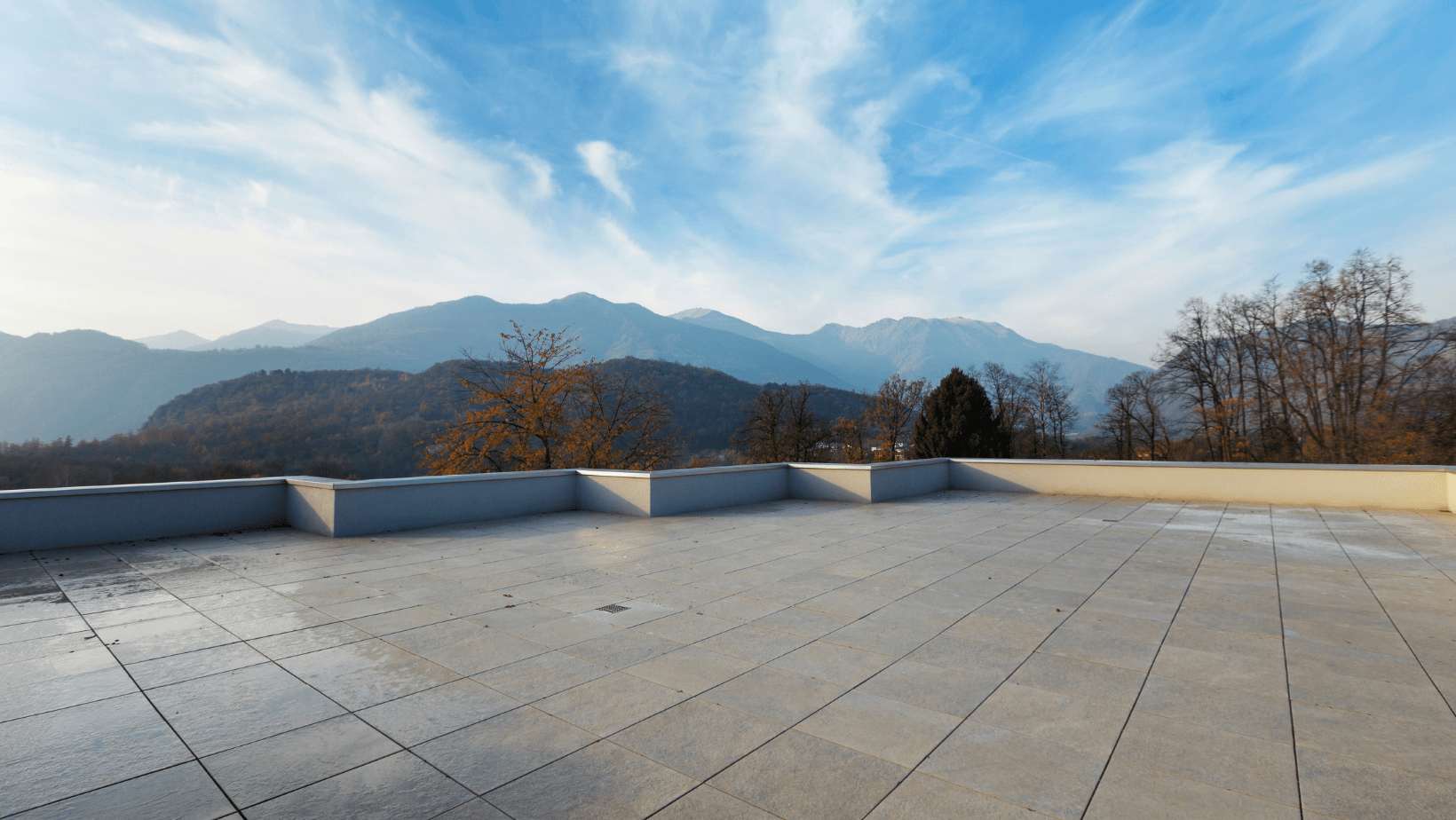  A panoramic view of a majestic mountain range seen from a rooftop, showcasing peaks against a clear blue sky.