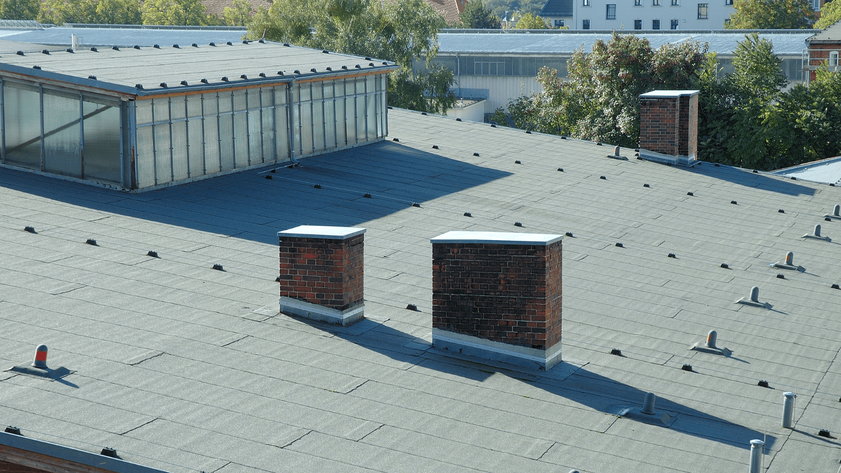 A rooftop featuring chimneys, with a building visible in the background against a clear sky.