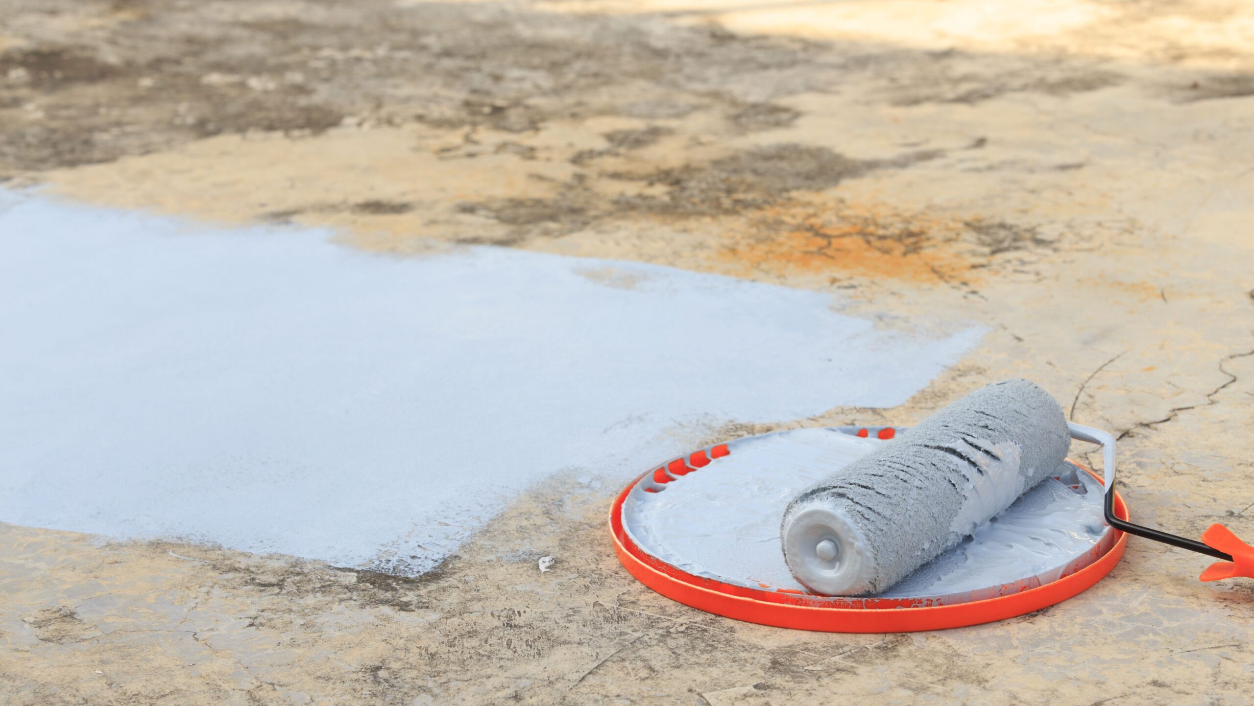 A person using a roller to apply paint on a concrete floor, showcasing the painting process in action.