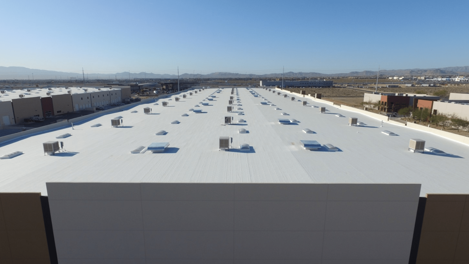 A large warehouse featuring multiple roofs under a clear blue sky, showcasing its expansive structure and open surroundings.