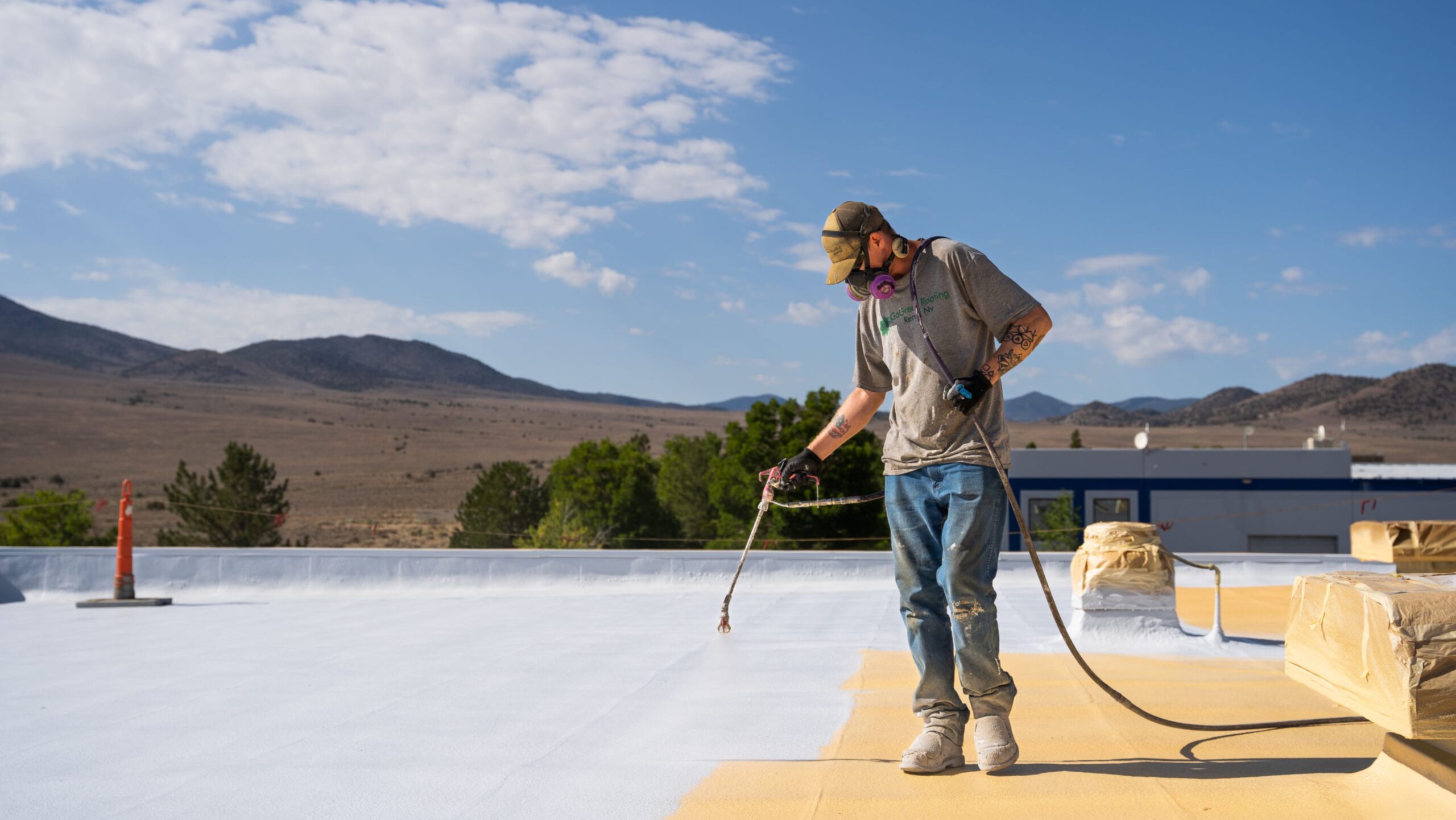 A man uses a hose to spray a white roof, ensuring proper maintenance and protection from the elements.