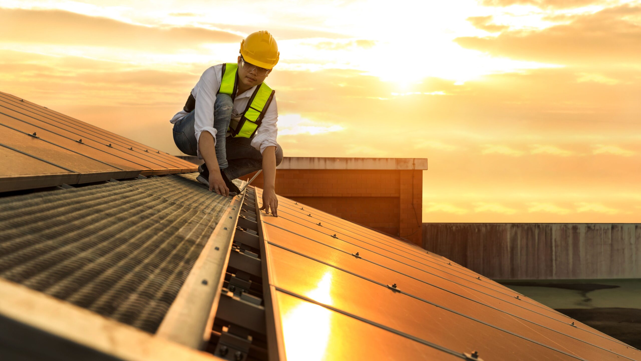 A man wearing a hard hat and safety vest is installing a solar panel, demonstrating commitment to renewable energy.