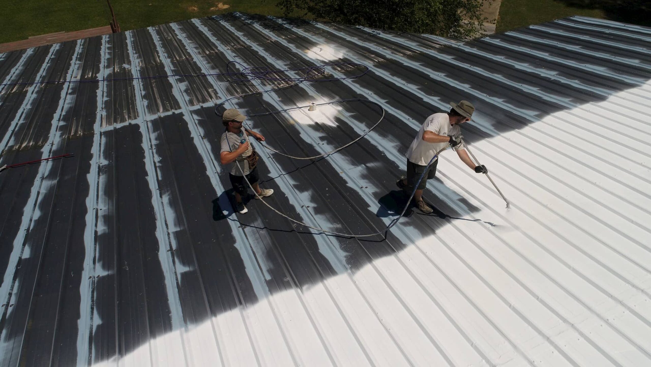 Two men in protective gear spray painting a metal roof, demonstrating teamwork and attention to detail.