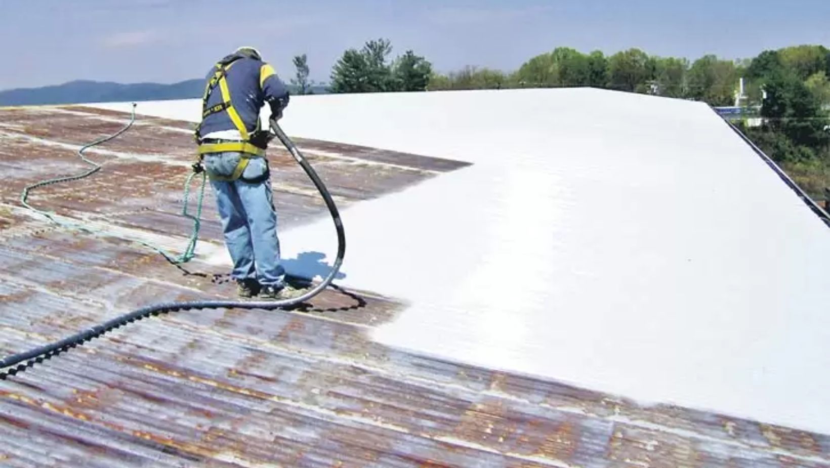 A man sprays white paint onto a roof