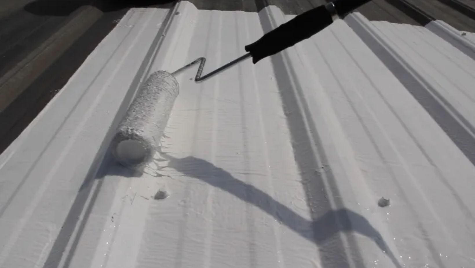 A person painting a metal roof with a paint roller
