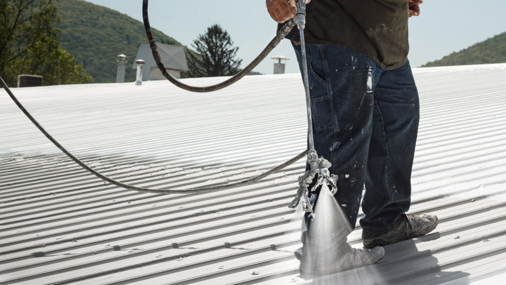 Worker using a spray gun to apply protective roof coating on a flat roof