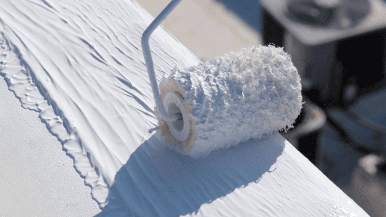 White paint roller applying protective roof coating to a flat roof surface