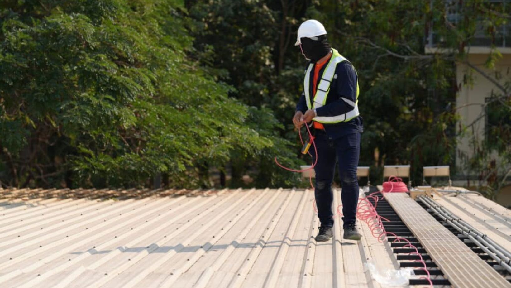 A man wearing a hard hat and safety vest stands on a roof
