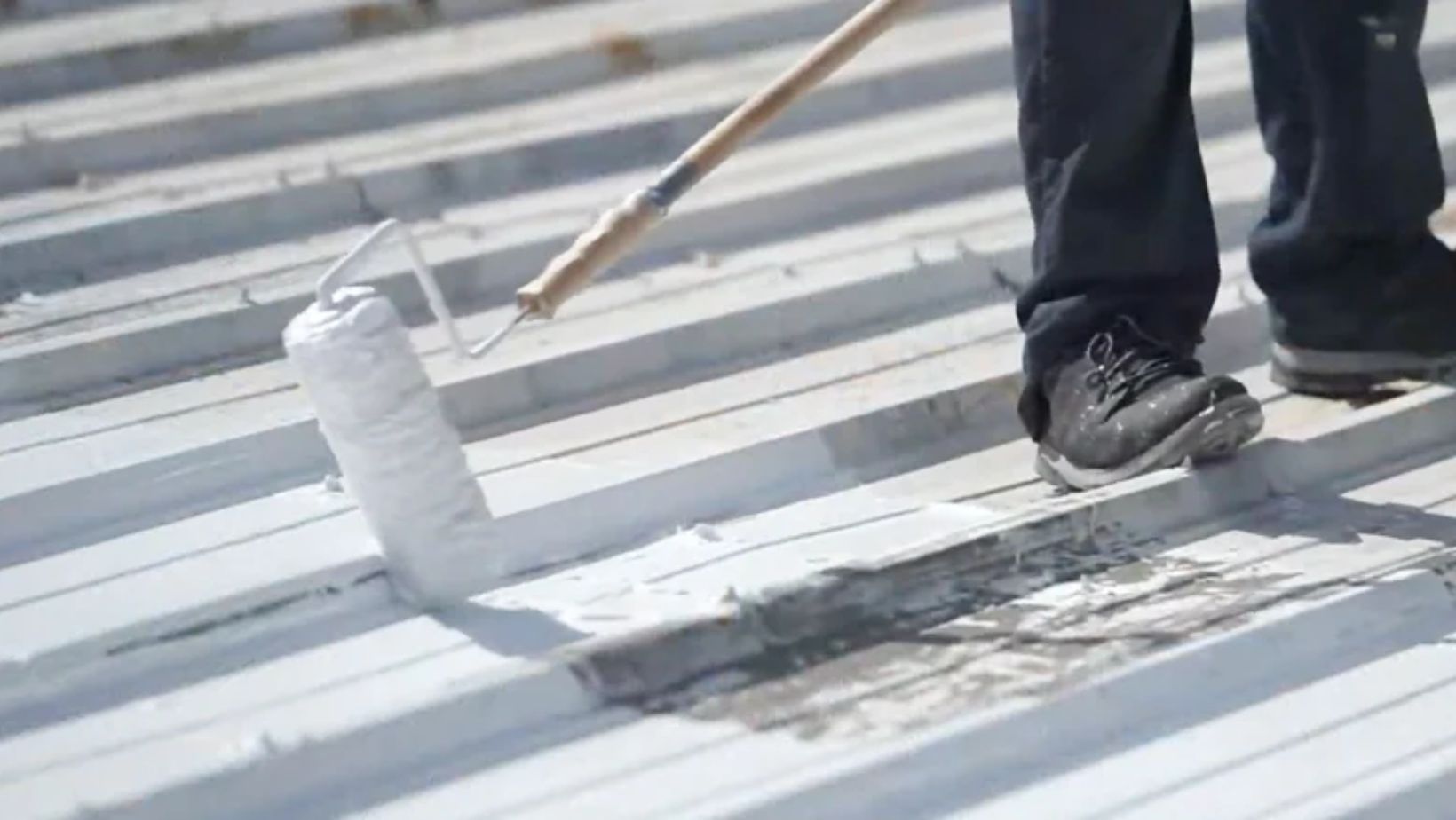 A person on a ladder painting a roof with a roller