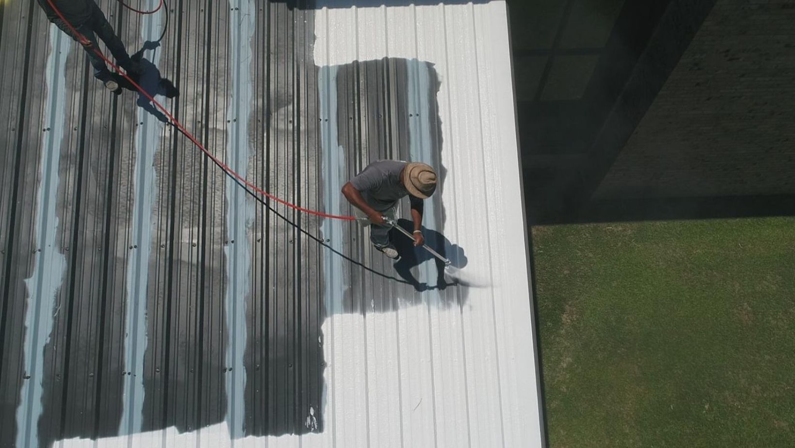 A man is applying paint to a metal roof using a hose