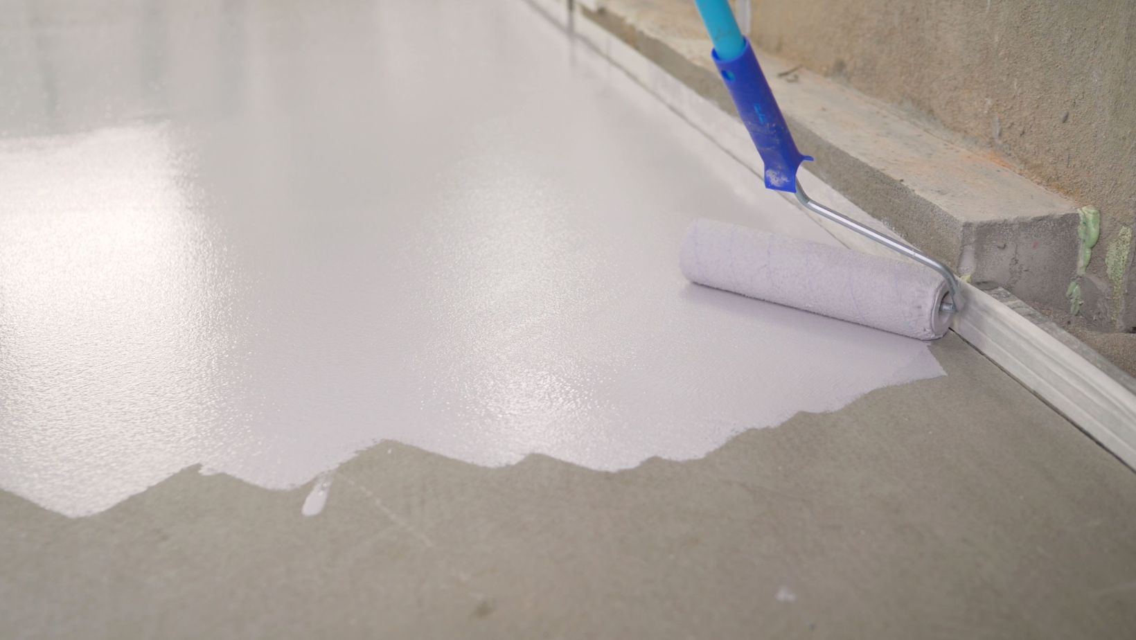 A person using a roller to apply roof coating on a floor.