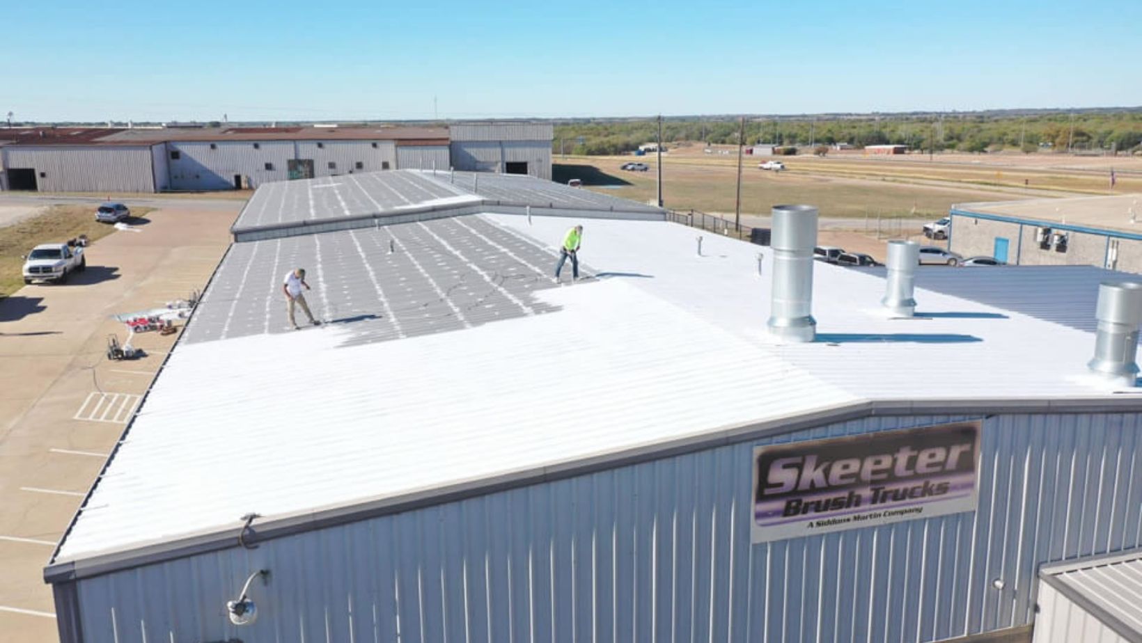 A person using a roller to apply roof coating on a floor.